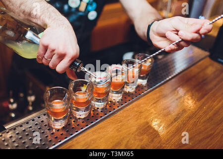 Bartender pouring strong alcoholic drink into small glasses on bar, shots Stock Photo