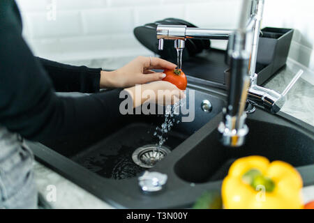Washed tomatoes under running water in a professional kitchen. Stock Photo