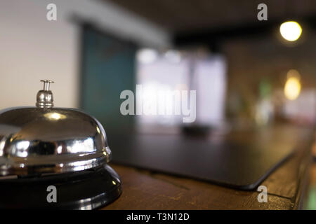 Service bell locating at reception. Silver call bell on table, receptionists on background. Stock Photo