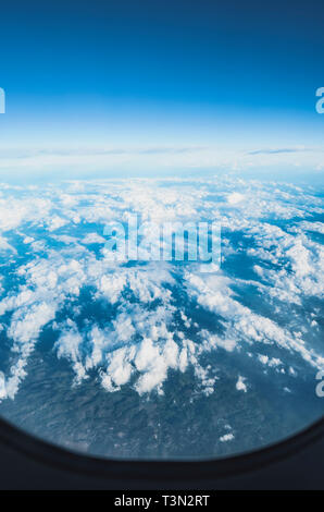 View of the sky above clouds over the earth through the airplane window, flying high. Deep blue sky with white clouds. Stock Photo
