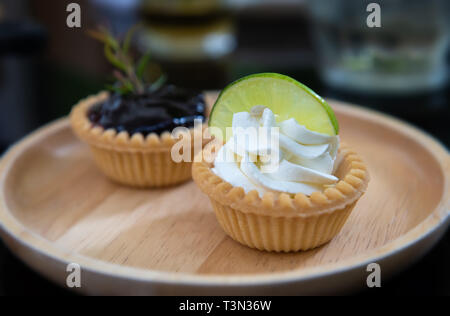 Mini fruits and cream pie tarts in wooden plate with indoor low lighting. Stock Photo