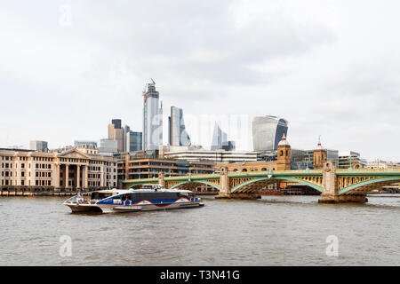Southwark Bridge and the City of London across the River Thames from Bankside, London, UK, a Thames Clipper river boat in the foreground,, April 2019. Stock Photo