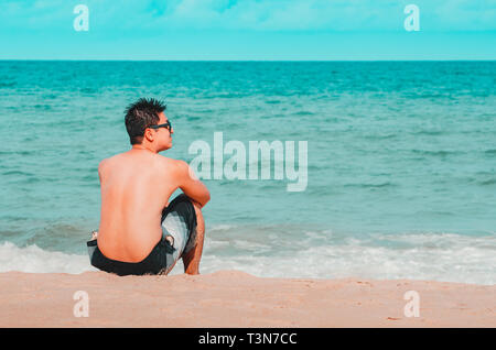 Man seated on the sand of the beach staring the sea. Cyan and orange tones. Photo at Praia de Tabatinga 2, Conde PB Brazil. Stock Photo