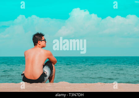 Man seated on the sand of the beach staring the sea. Cyan and orange tones. Photo at Praia de Tabatinga 2, Conde PB Brazil. Stock Photo