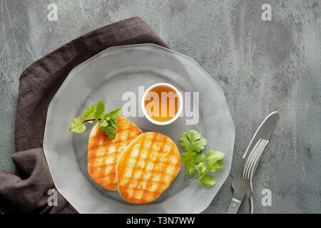 Grilled round slices of Greek cheese with honey, fresh mint and coriander leaves. Flat lay on dark grey table.