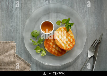 Grilled round slices of Greek cheese with honey, fresh mint and coriander leaves. Flat lay on light grey table.