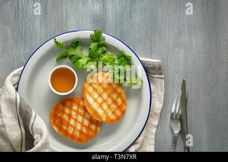 Grilled round slices of Greek cheese with honey, fresh mint and coriander leaves. Flat lay on light grey table.