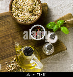 mix of cereals in a wooden bowl on a cutting board with olive oil, multicolored peppers and spices. food background home cooking on linen tablecloth Stock Photo