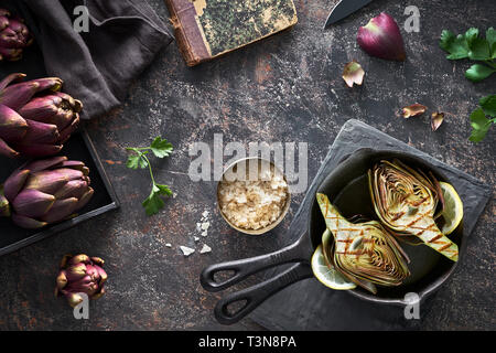 Flat lay with fresh and grilled red artishokes, whole and halved, on dark background Stock Photo