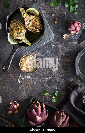 Flat lay with fresh and grilled red artishokes, while and halved, on dark background Stock Photo