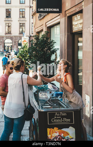 Strasbourg, France - Jul 22, 2017: Side view of young blonde woman serving customers with french bio home-made - ice-cream parlor in central Strasbourg France  Stock Photo