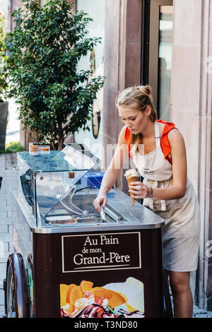 Strasbourg, France - Jul 22, 2017: Young blonde woman preparing a cone of fresh ice-cream for customer in city center of Strasbourg, Alsace Stock Photo