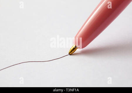 A closeup view of a pink ball point pen drawing an ink line on a textured paper surface. Stock Photo
