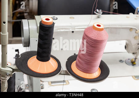 Two big black and pink bobbins with large mating threads mounted on a rod near the sewing machine on the table of the workshop in the studio fot car i Stock Photo