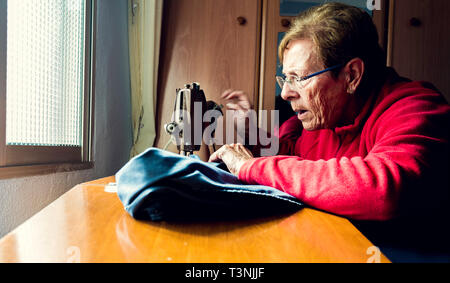 Senior woman using sewing machine concentrated with natural light coming through the window Stock Photo