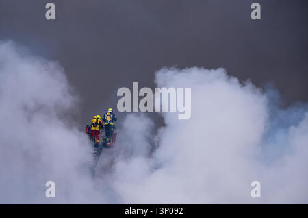 Roggendorf, Germany. 11th Apr, 2019. Firefighters extinguish a major fire in a peat factory from the basket of a turntable ladder. Several warehouses and production halls have gone up in flames there. Credit: Daniel Bockwoldt/dpa/Alamy Live News Stock Photo