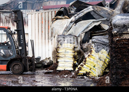 Roggendorf, Germany. 11th Apr, 2019. In a major fire in a peat factory, burnt pallets are transported away with bark mulch. Several warehouses and production halls have gone up in flames there. Credit: Daniel Bockwoldt/dpa/Alamy Live News Stock Photo
