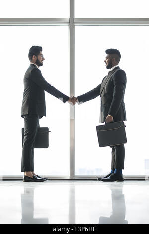 Full length side view of businessmen shaking hands in office Stock Photo