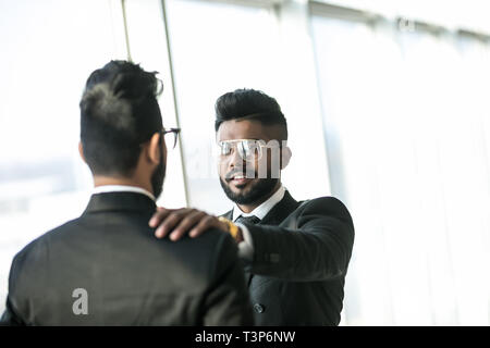 Happy handsome indian businessman shaking hands on business deal at office. Hand on shoulder, side view, copyspace, suit. Stock Photo