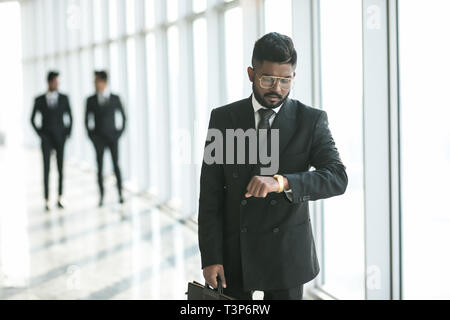 Busy businessman looking at wristwatch while hurrying on meeting in office. Young man in business suit checks time left to end of work day. Entreprene Stock Photo