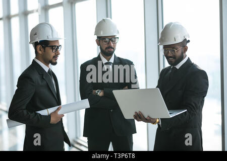Three businessmen in ties and hardhats surprised with window scene. Property investor visiting site and impressed with neighboring construction. Stock Photo