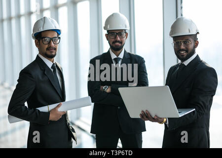 Three businessmen in ties and hardhats surprised with window scene. Property investor visiting site and impressed with neighboring construction. Stock Photo