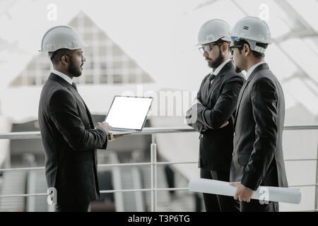 Three businessmen in ties and hardhats surprised with window scene. Property investor visiting site and impressed with neighboring construction. Stock Photo