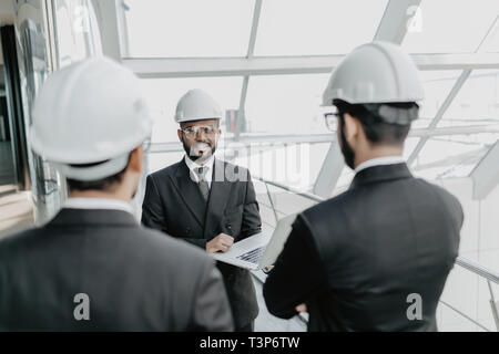 Engineering men with paper and hardhat working indoors in building . Team of architects working together on business plan. Work group of three develop Stock Photo
