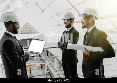Engineering men with paper and hardhat working indoors in building . Team of architects working together on business plan. Work group of three develop Stock Photo