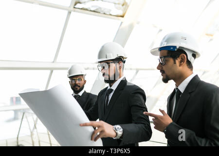 Qualified young architects are standing and discussing plan of building. They are looking with interest at blueprint while foreman is pointing finger  Stock Photo
