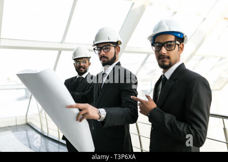 Closeup of three indian business people wearing helmets and standing at new modern building background. Architects concept. Stock Photo