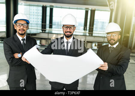 Qualified young architects are standing and discussing plan of building. They are looking with interest at blueprint while foreman is pointing finger  Stock Photo