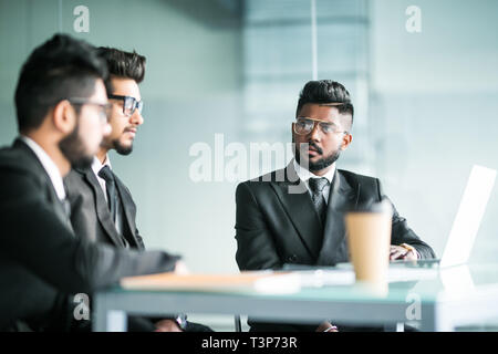 Three indian businessmen working together talking collaborate on laptop in office. Three Male business team discuss online project presentation corpor Stock Photo