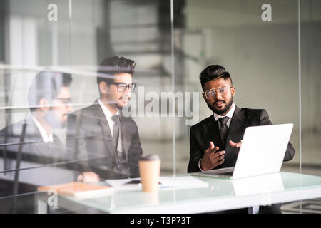Three indian businessmen working together talking collaborate on laptop in office. Three Male business team discuss online project presentation corpor Stock Photo