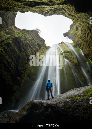 Gljufrafoss (Gljufrabui) waterfall in gorge of mountains. Tourist attraction Iceland near falls of Seljalandsfoss. Man hiker in blue jacket standing o Stock Photo