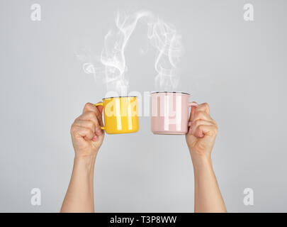 two raised hands up with ceramic cups, thick steam comes out of the mug and connects, love concept Stock Photo