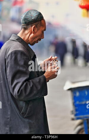 Thin-bearded Uyghur man eating a mutton skewer-Hotan's Sunday market. Xinjiang-China-0091 Stock Photo