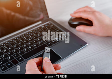 Hand of a woman holding a USB device connected to Laptop computer on white table Stock Photo