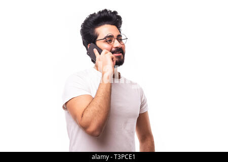 Image of happy young bearded emotional man standing over white wall background isolated. Looking aside while talking by phone. Stock Photo