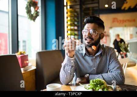 Handsome man eat salad holding fork in one hand in cafe