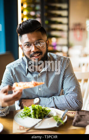 Handsome man holding and eat piece pizza and salad in cafe