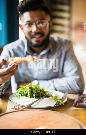 Handsome man holding and eat piece pizza and salad in cafe