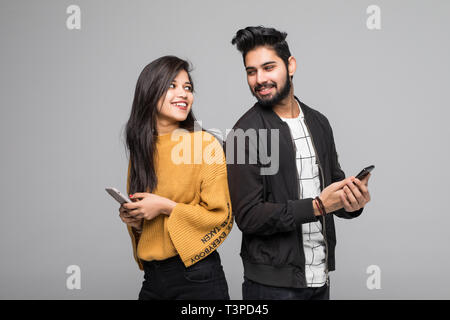 Beautiful young asian couple holding mobile phones and standing back to back against grey background Stock Photo