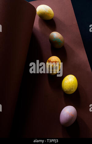 Colored eggs on a brown background , brown and black background, text " happy easter" Stock Photo