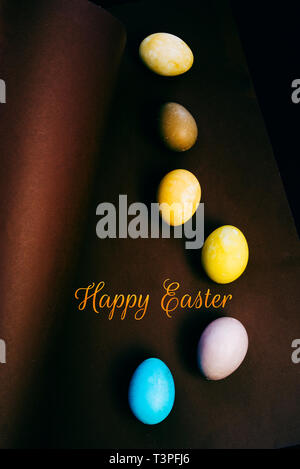 Colored eggs on a brown background , brown and black background, text " happy easter" Stock Photo