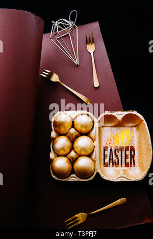 Golden eggs on a brown background with gold cutlery, brown and black background, text " happy easter" Stock Photo
