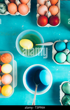 Dyeing eggs for Easter holidays, coloring eggs with different color and tonality using food colorant over a blue concrete background Stock Photo