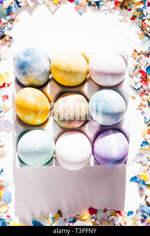Colored eggs container with different colored egg, circled by pieces of broken eggs,  easter concept, hard natural direct light Stock Photo