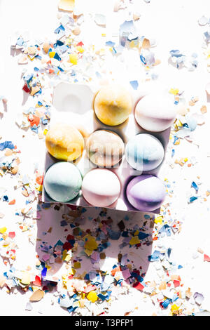 Colored eggs container with different colored egg, circled by pieces of broken eggs,  easter concept, hard natural direct light Stock Photo