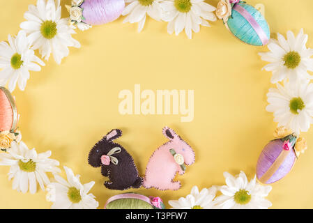 Easter eggs, bunnies, and daisies in wreath on solid pastel yellow background Stock Photo